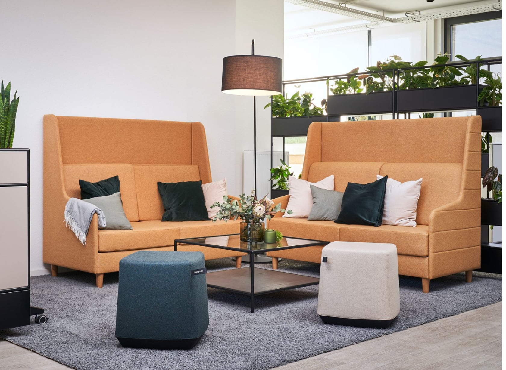 Inviting conversation space with two orange couches featuring privacy walls and adorned with decorative pillows. The sofas are accompanied by blue and beige ottomans to create a cozy space for collaboration.